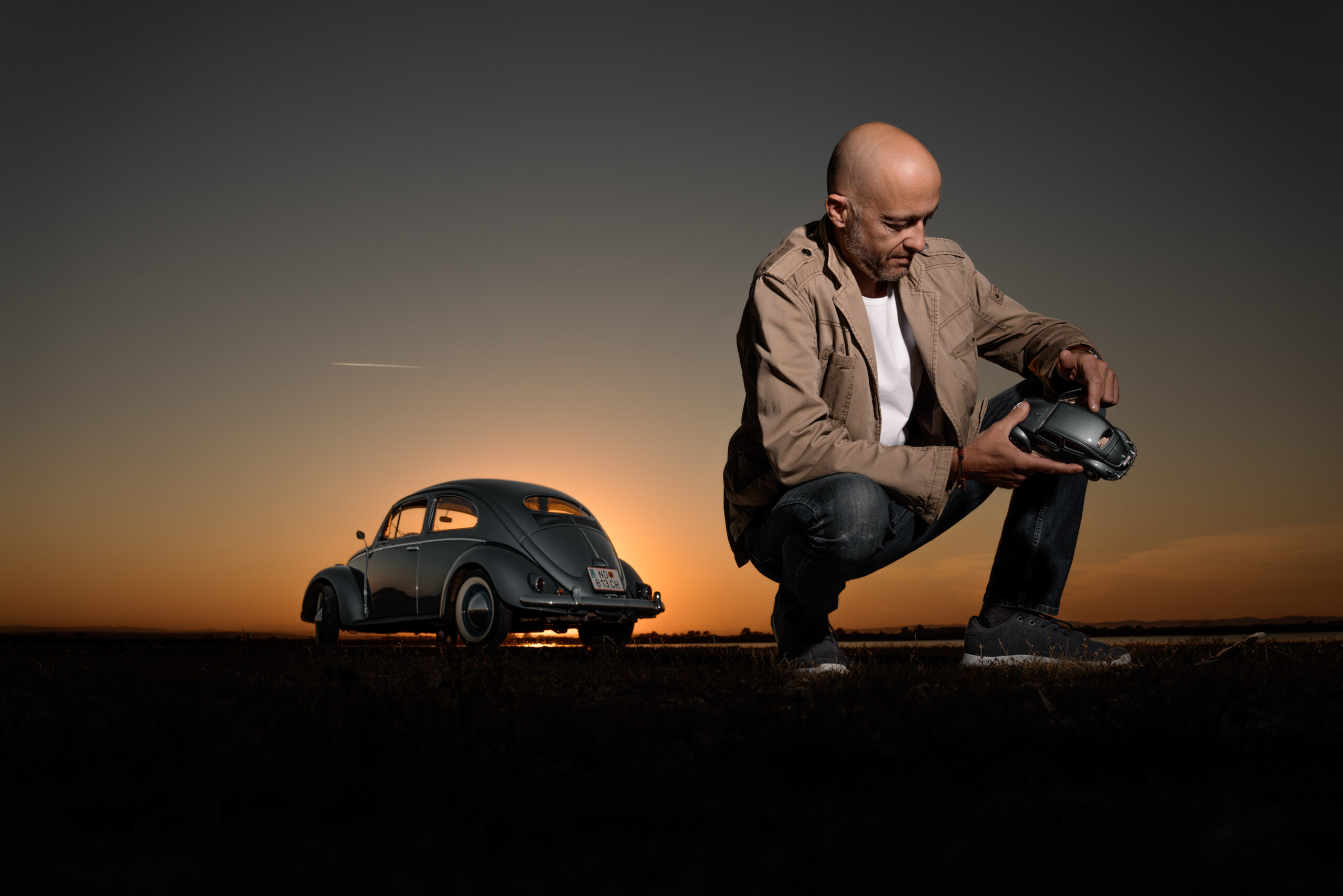 Nikolaus Eberstaller hockt vor seinem VW Käfer und betrachtet ein Modellauto